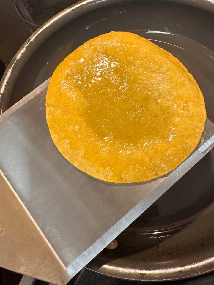 A corn tortilla which had been fried in lard, on top of a large spatula.