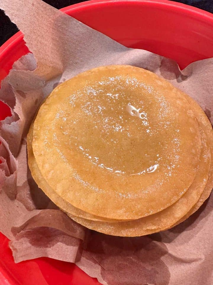 A stack of corn tortillas which had been fried in lard, placed to drain on paper towels in a red container.