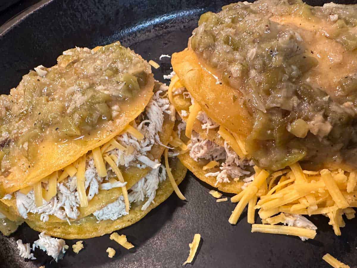 Corn tortillas dipped in green chile sauce stacked on top of each other and filled with shredded chicken and cheese. The top layer is a corn tortilla and green chile sauce.