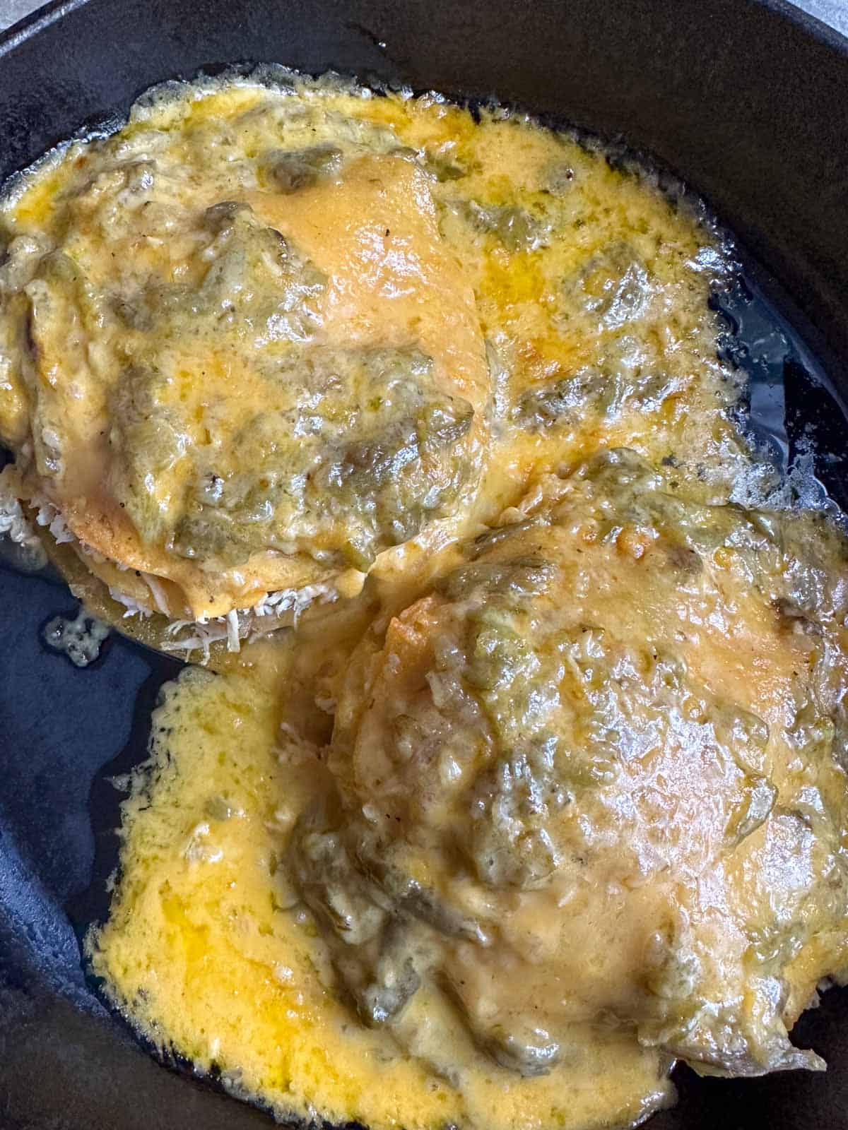 Green chile stacked chicken enchiladas smothered with melted cheese in a cast iron skillet.