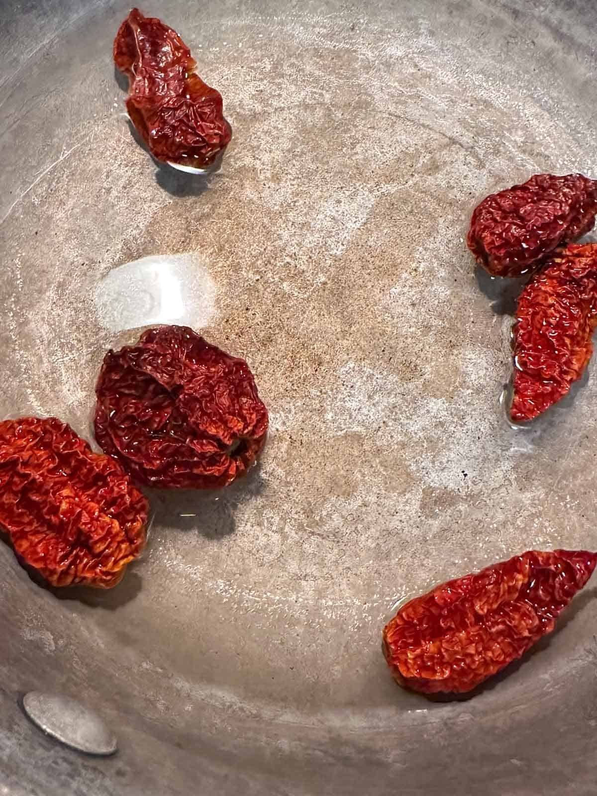 Dried ghost peppers being rehydrated in warm water in a saucepan.