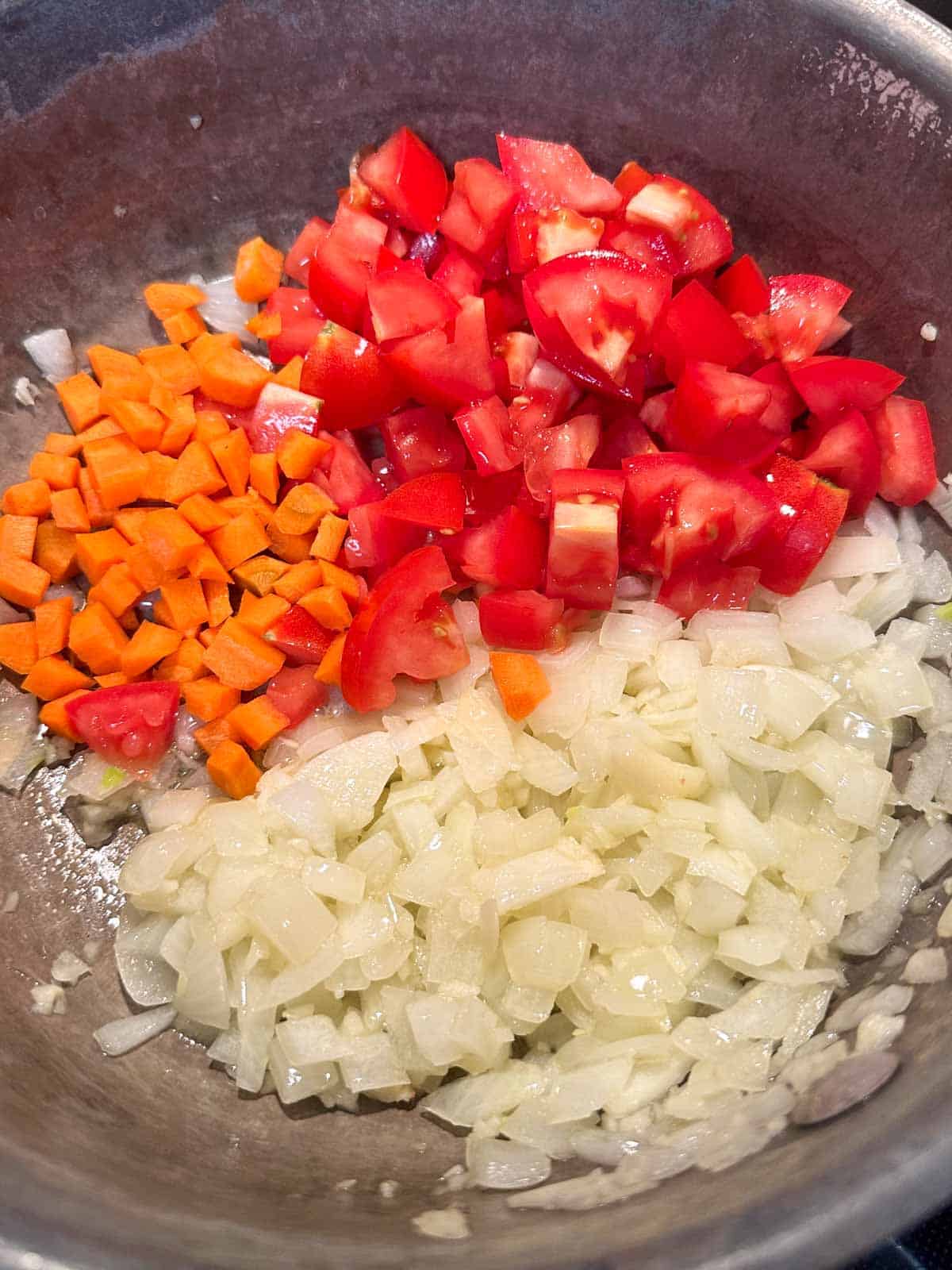 Chopped onion, tomatoes and carrot in a saucepan.