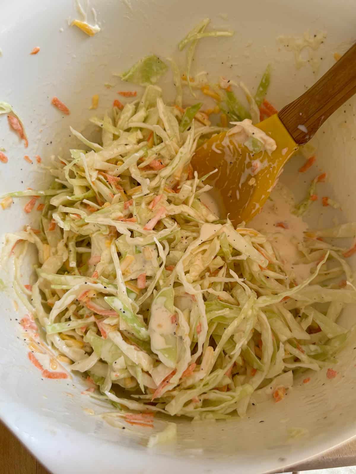 A mixing bowl containing coleslaw with a yellow spoon in the mixing bowl.