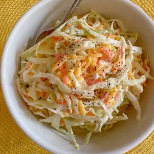 A bowl containing coleslaw and there is a fork in the bowl.