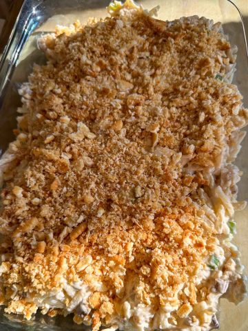 A large casserole dish containing a cheesy shredded hash brown mixture topped by crushed Ritz crackers.