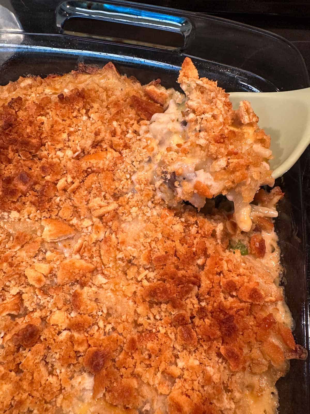 A large casserole dish containing a cheesy shredded hash brown mixture topped by crushed Ritz crackers which has just come out of the oven. There is a blue spoon containing some of the dish which it has scooped up.