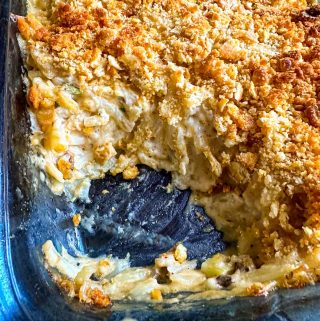 A large casserole dish containing a baked cheesy potato casserole with a browned topping consisting of crushed Ritz crackers. A scoop has been taken out of the casserole so that the inside creamy part of the casserole can be seen.
