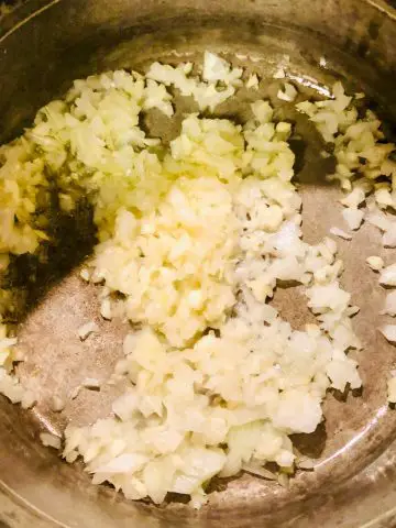 A saucepan containing minced onion and garlic.