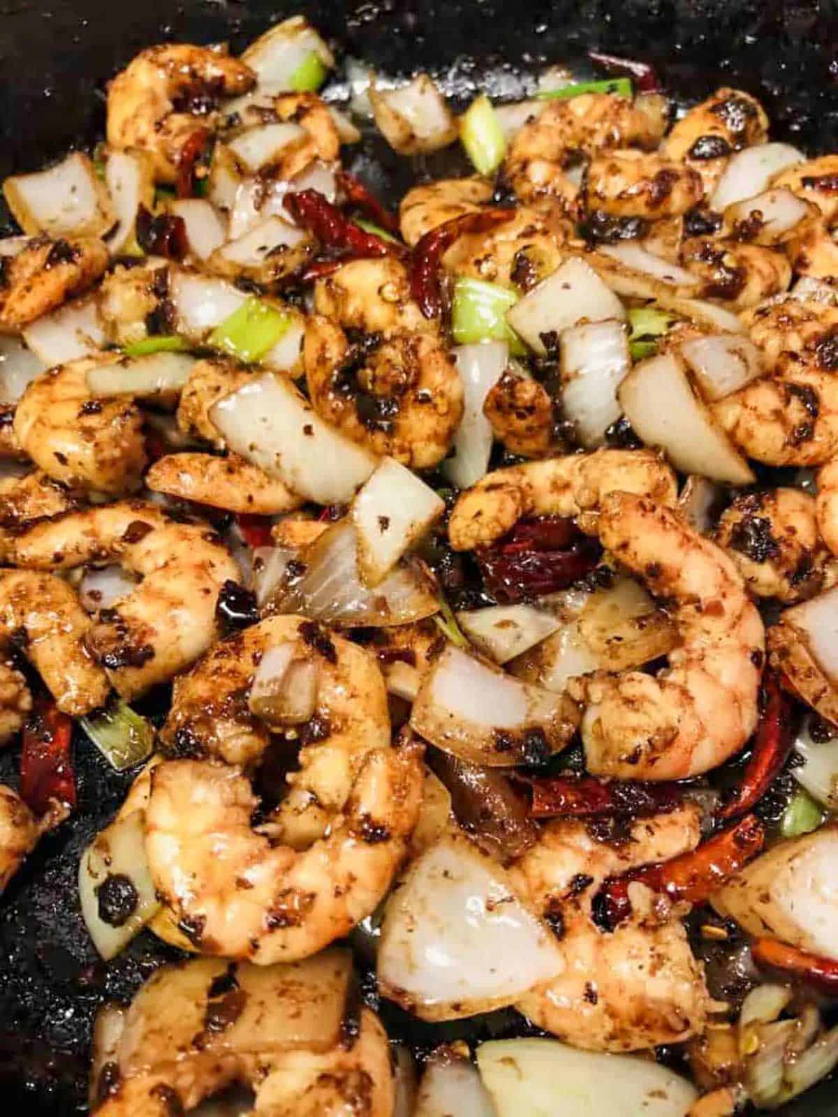 Shrimp With Black Bean Sauce with onions, green onions, and dried red chilies in a cast iron pan.