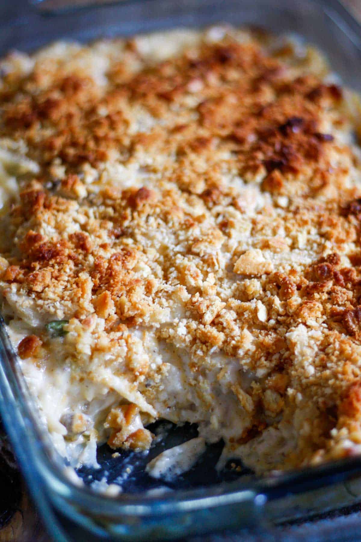 A large casserole dish containing a baked cheesy potato casserole with a browned topping consisting of crushed Ritz crackers. A scoop has been taken out of the casserole so that the inside creamy part of the casserole can be seen.