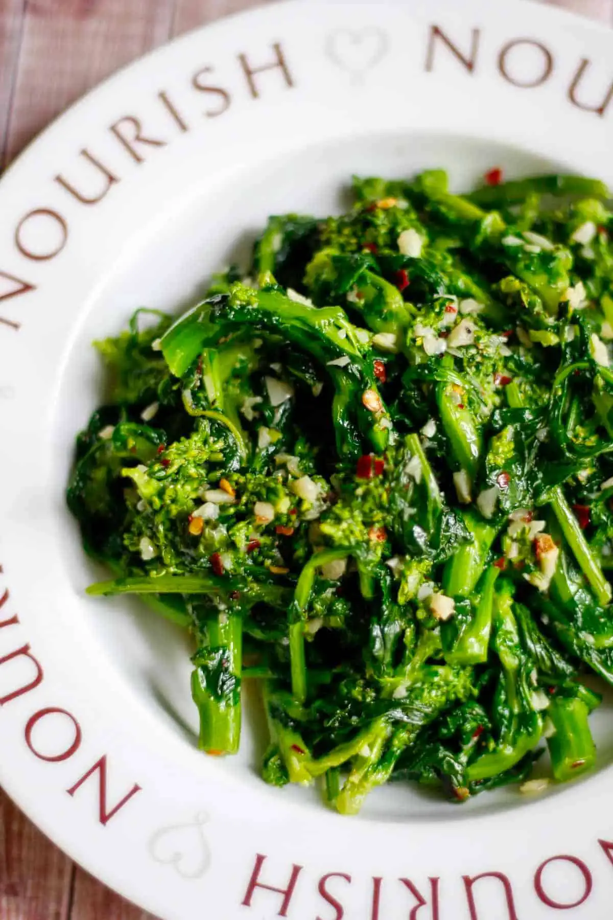 Sautéed broccoli rabe also known as rapini in a dish with the word "Nourish" repeated on the rim of the dish.