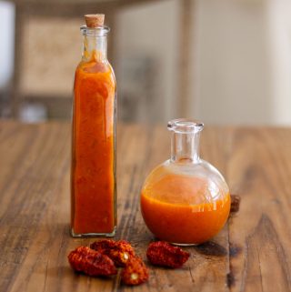 Glass bottles containing homemade ghost pepper hot sauce and some dried ghost peppers in front of the glass bottles.