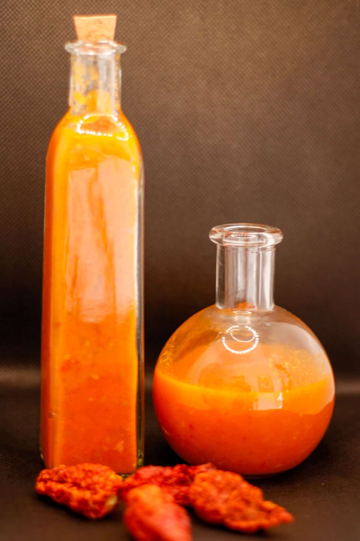 Glass bottles containing homemade ghost pepper hot sauce and some dried ghost peppers in front of the glass bottles.