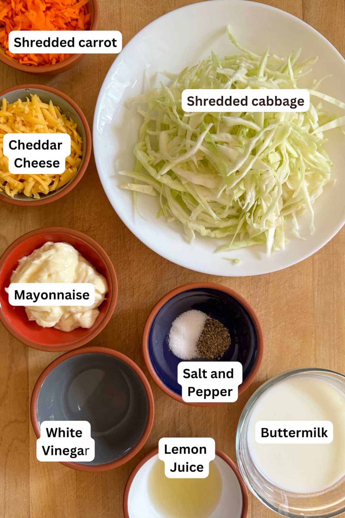 The ingredients needed for this coleslaw including shredded carrot and cabbage, cheddar cheese, mayonnaise, salt and pepper, white vinegar, lemon juice, and buttermilk.