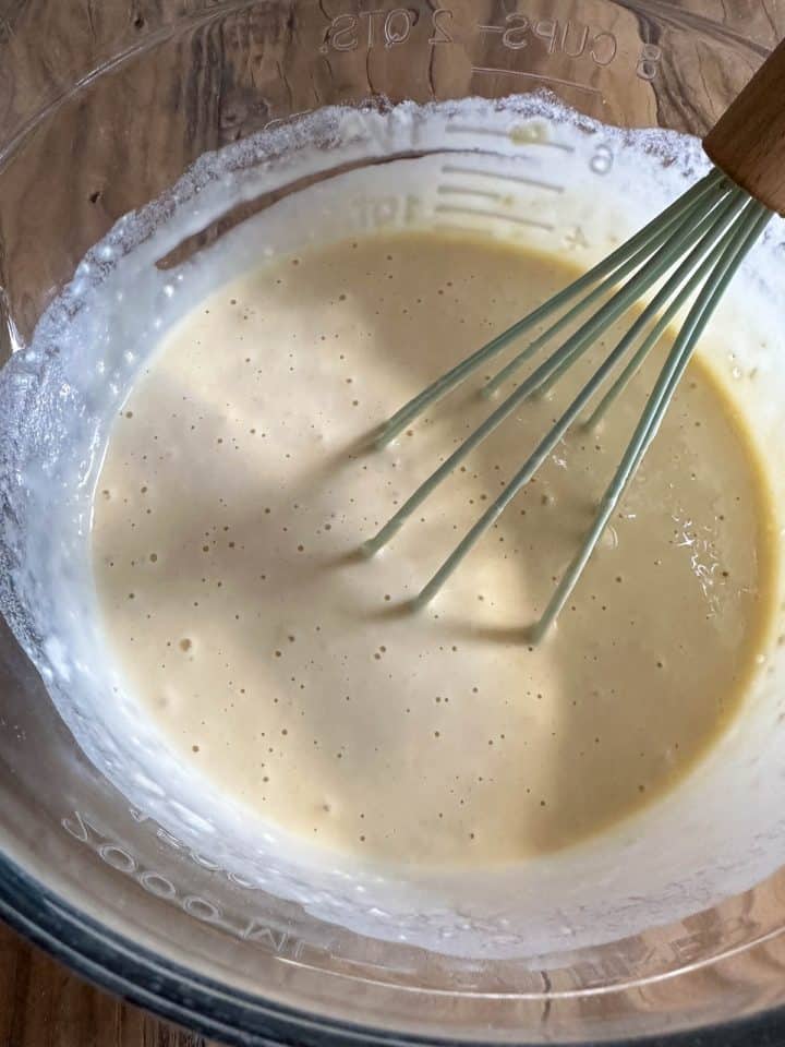 A glass bowl containing batter and a whisk.