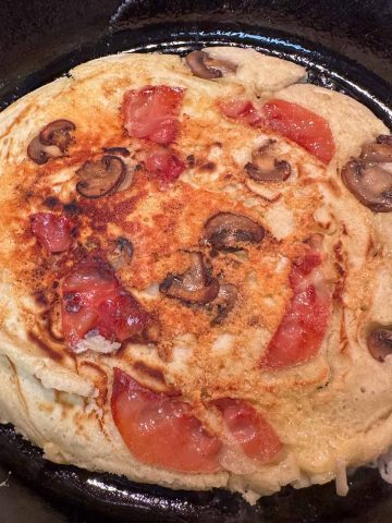 A cast iron skillet containing a savory pancake with mushrooms, prosciutto, and gouda.