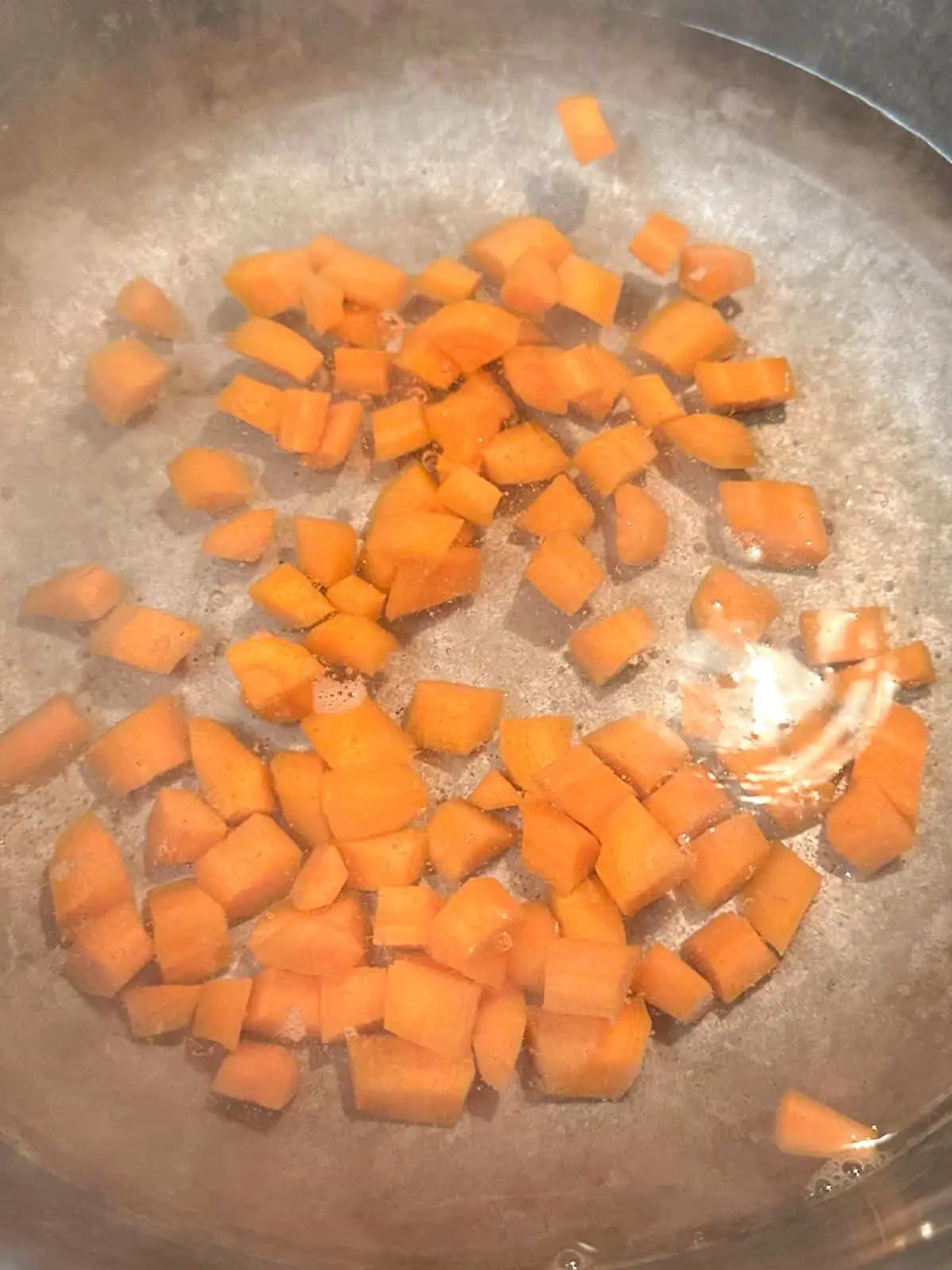 A saucepan with cut up pieces of carrot covered with water.