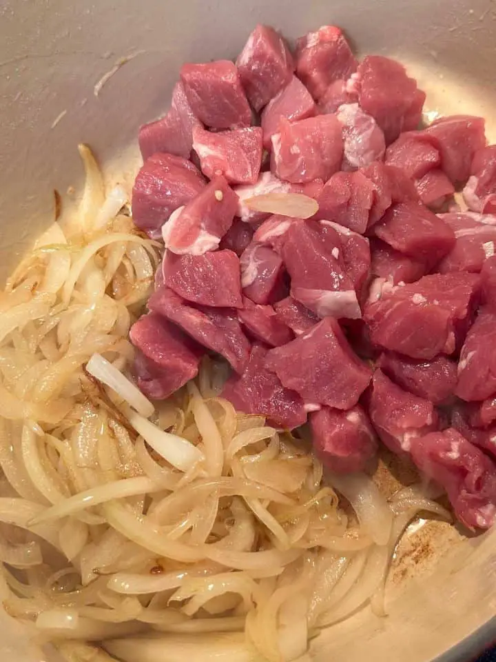 Chunks of raw pork tenderloin and sliced onions in a Dutch oven.