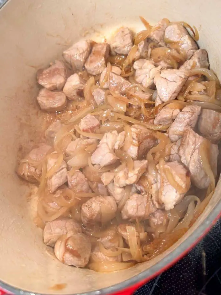 Chunks of pork tenderloin and sliced onions cooking in a Dutch oven.