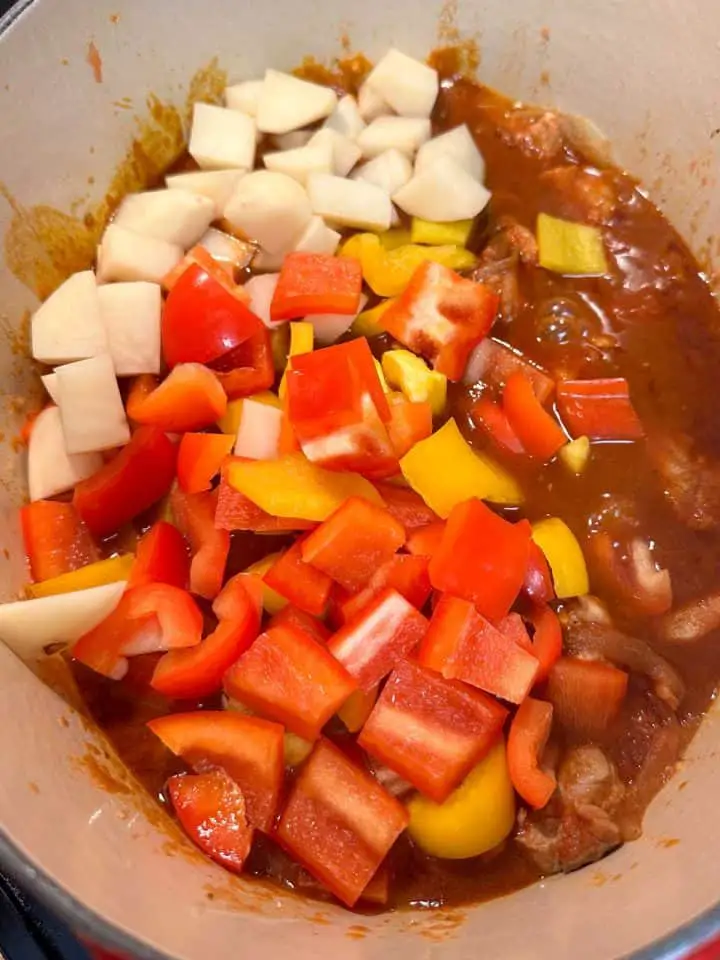 Red and yellow bell peppers and cut up potatoes added to a Hungarian pork goulash stewing in a Dutch oven.