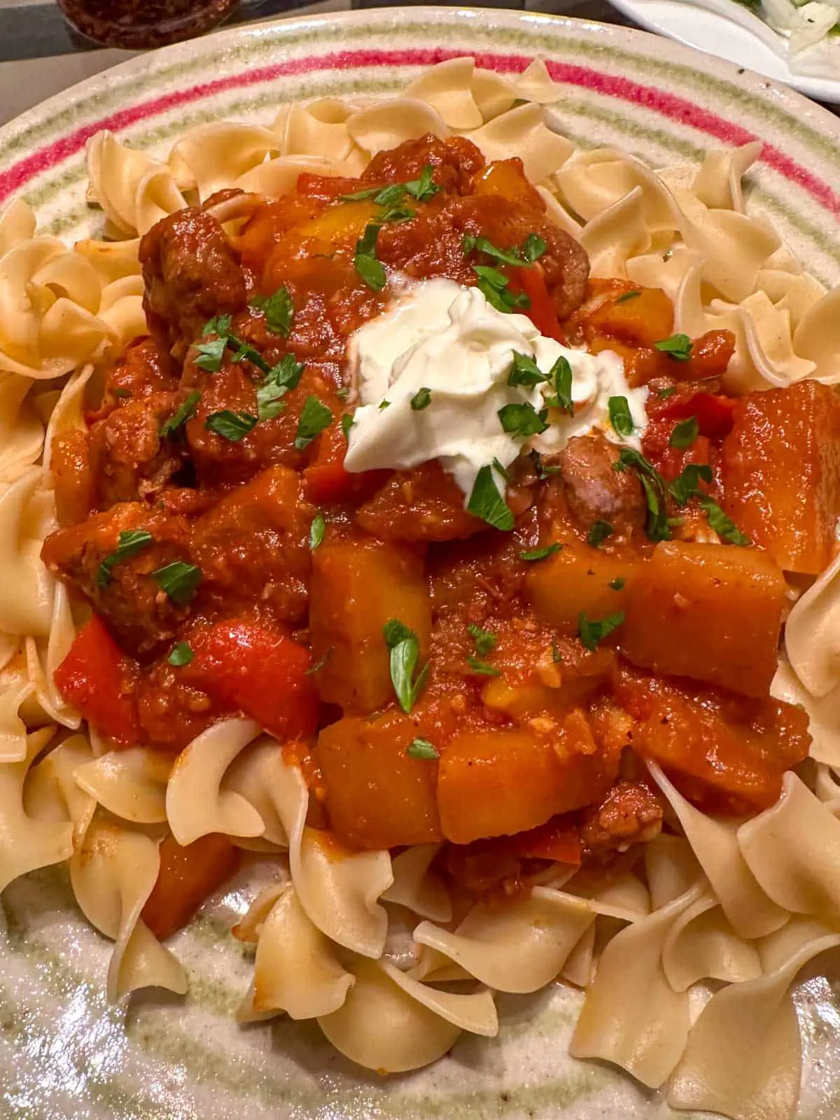 Hungarian Pork Goulash atop egg noodles garnished with sour cream and parsley.