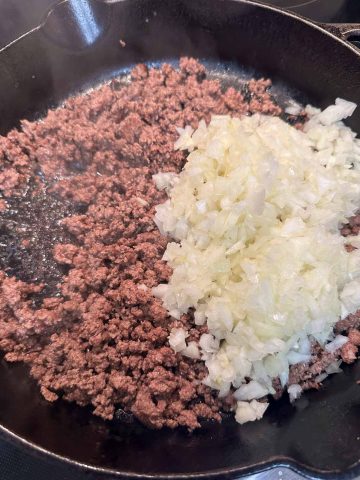A cast iron skillet containing cooked ground beef and diced onions.