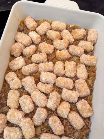 A white casserole dish containing a tater tot casserole with frozen tater tots.