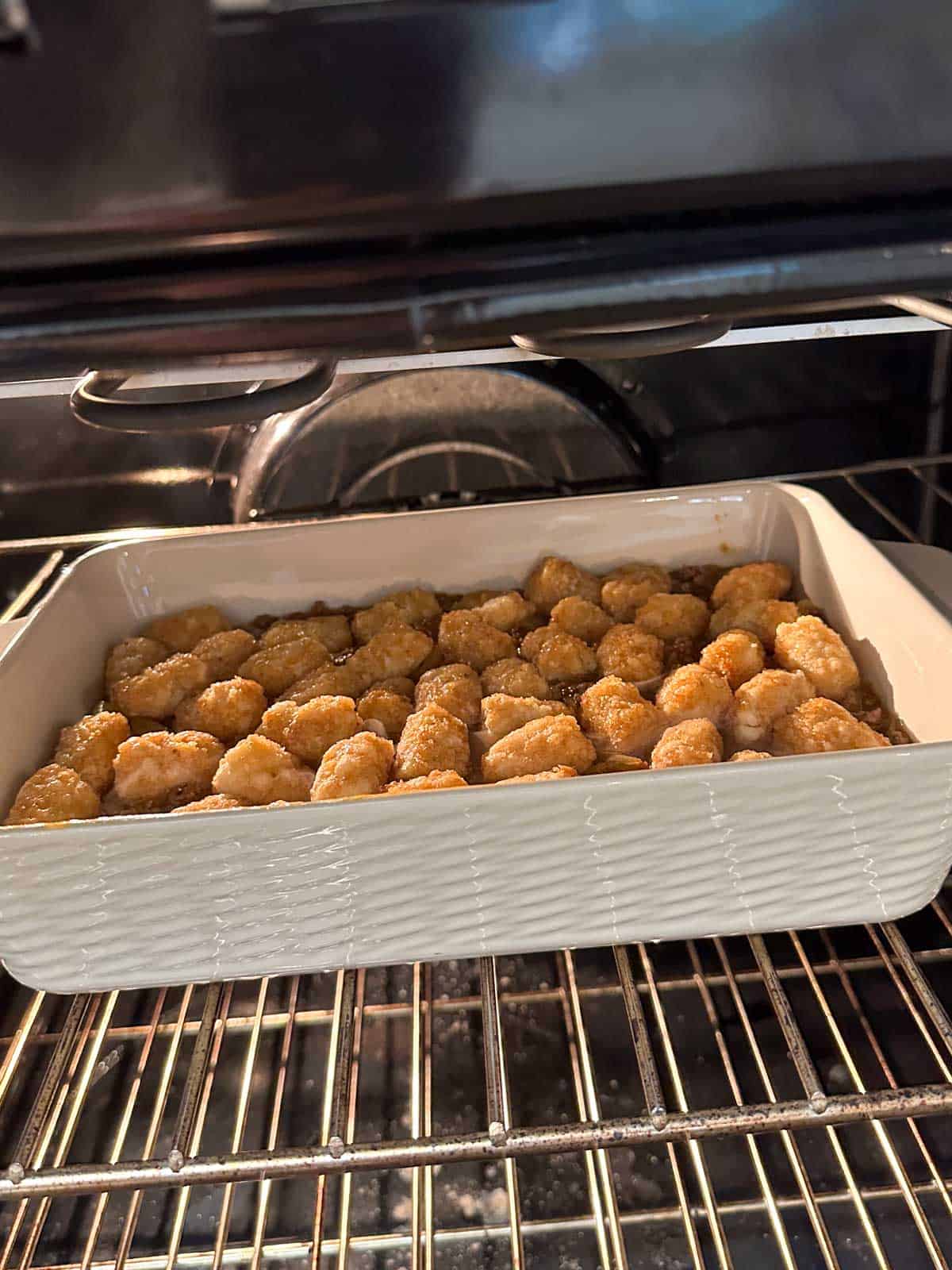 A white casserole dish with a tater tot casserole cooking in the oven.