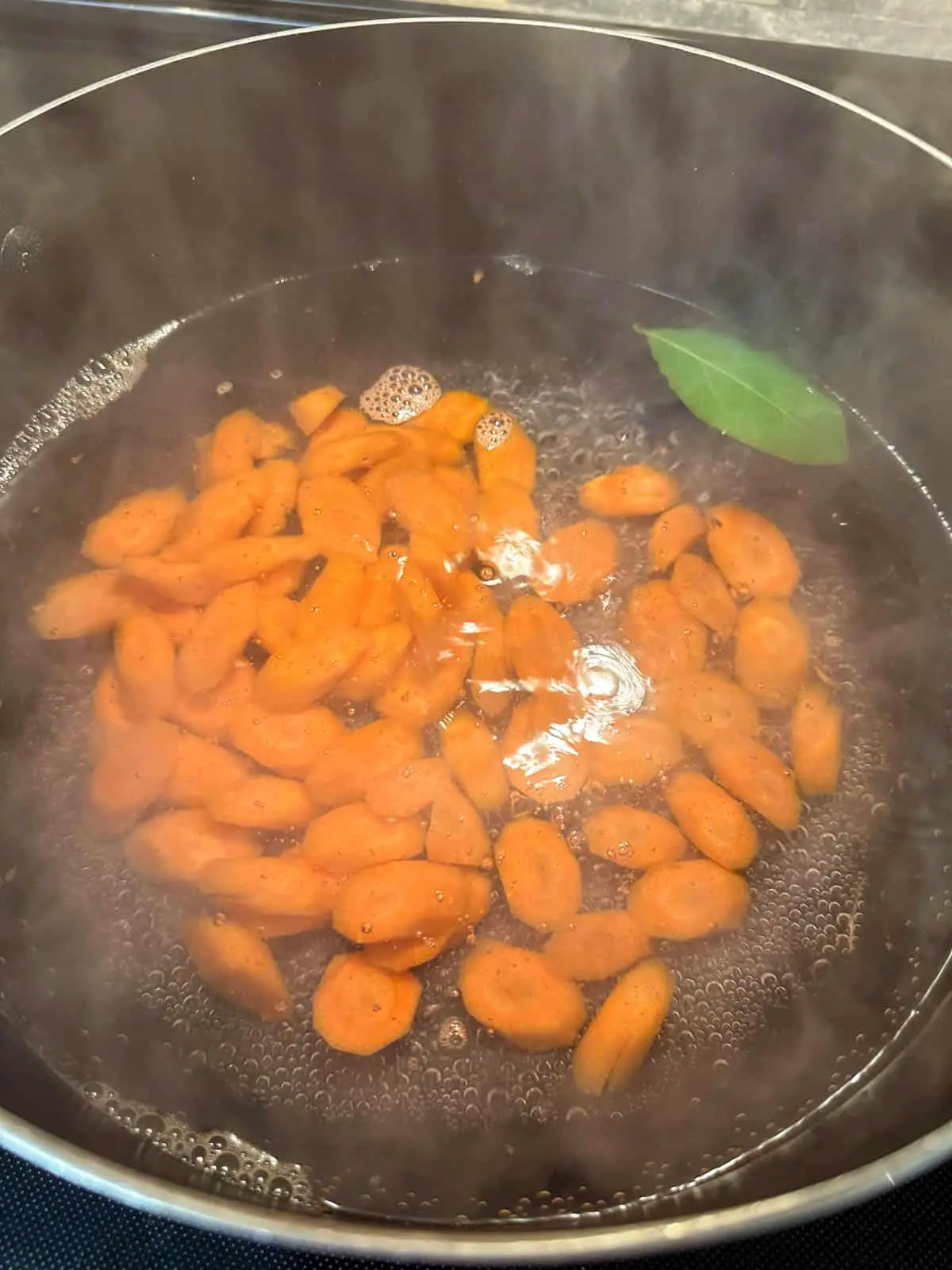 Sliced carrots and a bay leaf in a pot of boiling water.
