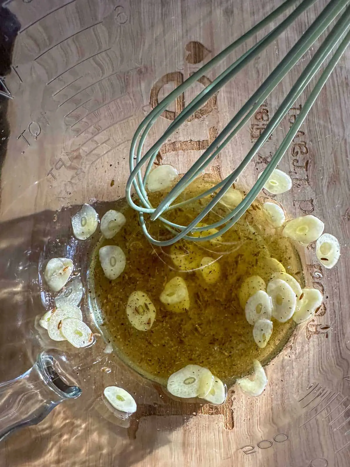 Sliced garlic, olive oil, cumin seeds, salt and pepper in a glass bowl with a whisk.