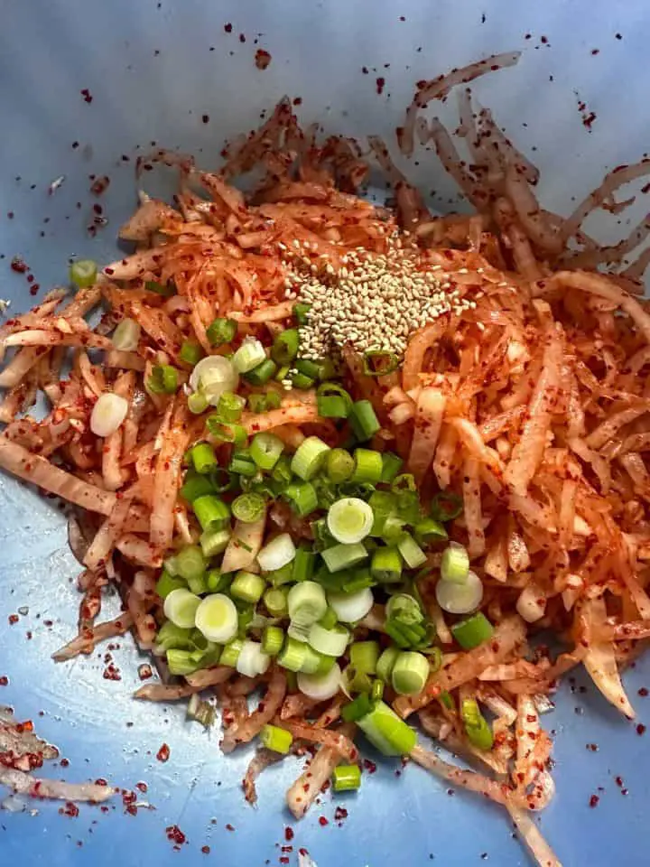 Korean radish salad which is julienned daikon radish in a spicy red sauce with sesame seeds and green onions added on top of the shredded radish.