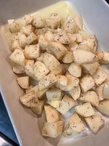 Bite sized pieces of potato seasoned with salt and pepper in a dish with melted chicken fat.