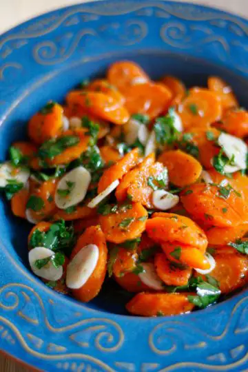 Portuguese Marinated Carrots which is sliced carrots, sliced garlic, seasonings and chopped cilantro in a blue bowl.