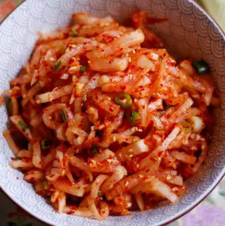 Korean radish salad which is julienned daikon radish in a spicy red sauce garnished with green onions and sesame seeds in a bowl.