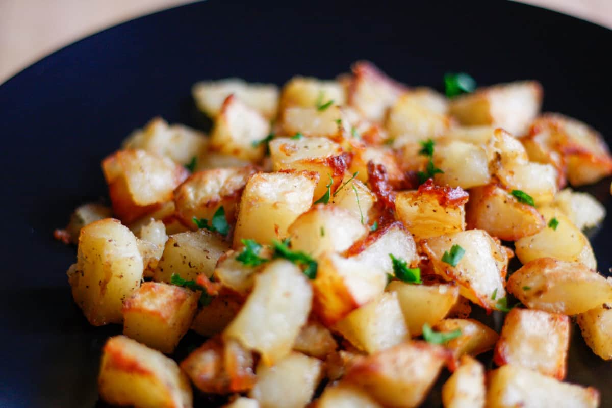 Crispy roasted potatoes garnished with minced parsley on a black plate.