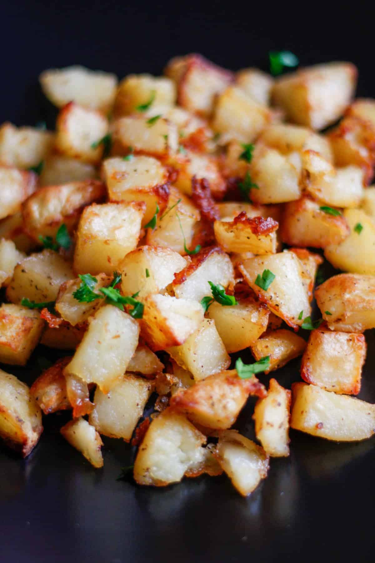 Crispy roasted potatoes garnished with minced parsley on a black plate.
