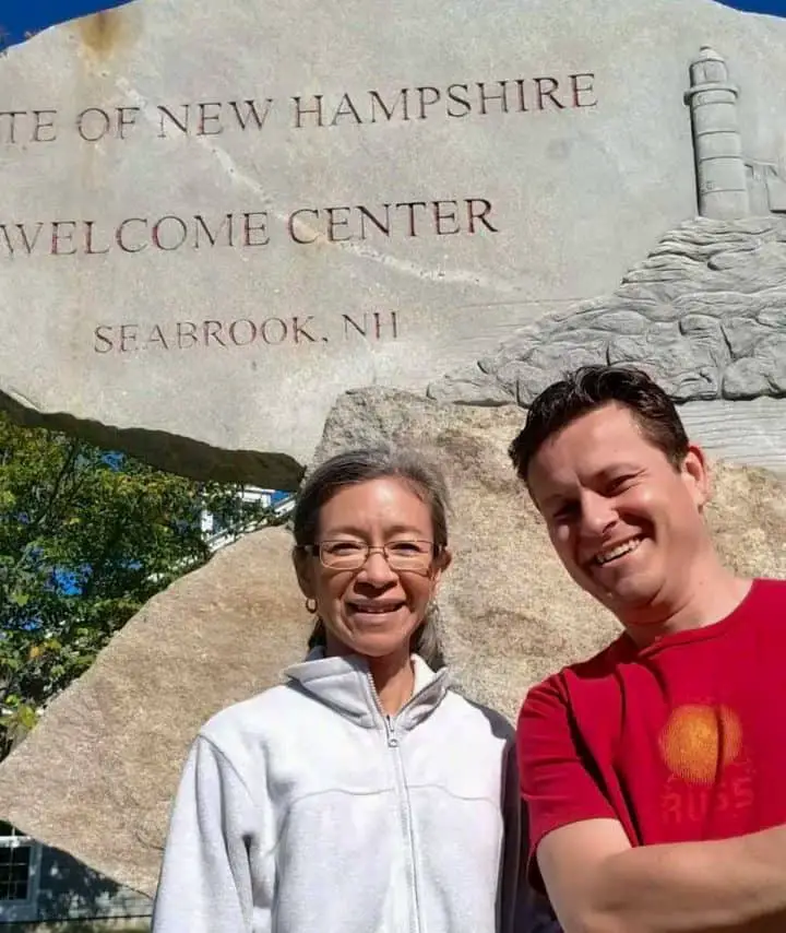 A man and woman standing in front of a sign that says "State of New Hampshire Welcome Center, Seabrook, NH."