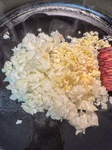 Minced garlic and onion in a cast iron pan. There is a glimpse of a wooden utensil in the picture.