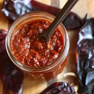 Red Chile Sauce in a glass jar with a spoon and red chile pods in the background.