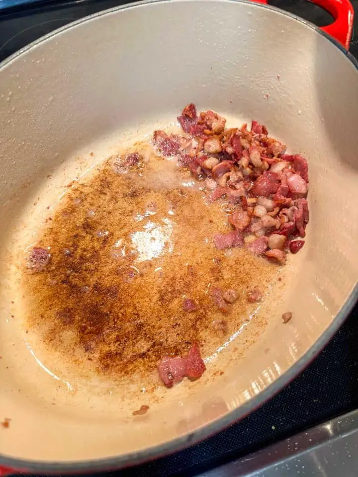 A Dutch oven containing bacon fat and bacon bits.