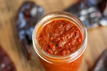 Red Chile Sauce in a glass jar and red chile pods in the background.