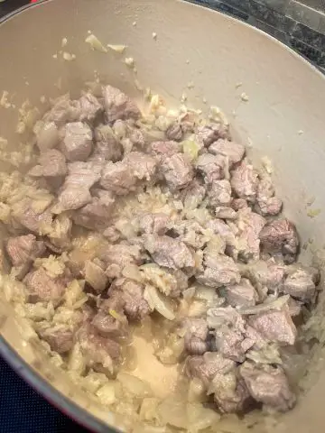 Pieces of pork tenderloin cooked until no longer pink along with diced onion and garlic in a Dutch oven.