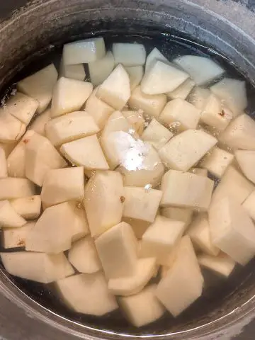 Cut up pieces of Russet potatoes covered by water in a saucepan.