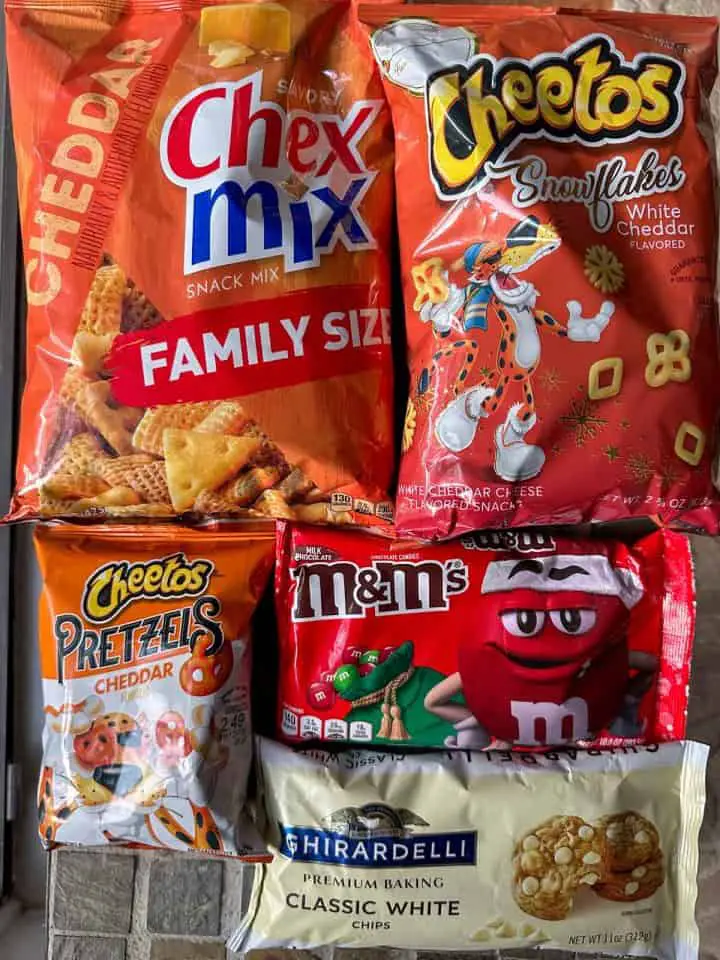 Bags of Cheddar Chex Mix, Snowflakes Cheetos, Cheetos cheddar pretzels, Christmas M&M's, and Ghirardelli Classic White Chips.