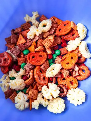 Red and green M&M's, Chex Mix, Cheetos Pretzels and Cheetos snowflakes in a blue bowl.