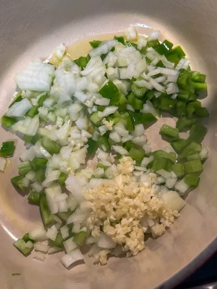Chopped green bell pepper, onion, and celery in olive oil in a Dutch oven. There is also minced garlic in the Dutch oven.