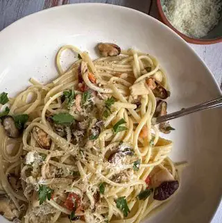 Linguine with seafood mix garnished with Italian parsley and Parmesan cheese in a pasta bowl. There is a fork resting in the pasta and a small bowl with Parmesan is in the background.