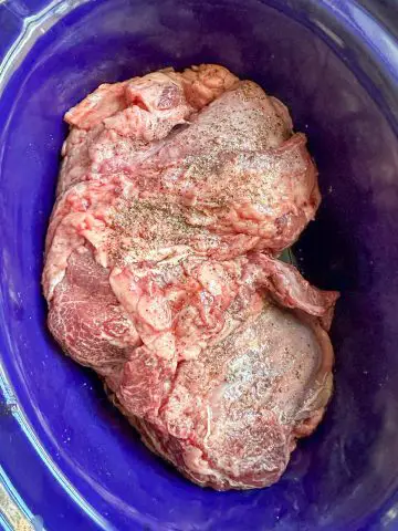 Beef cheek meat seasoned with salt and pepper in a crockpot dish.