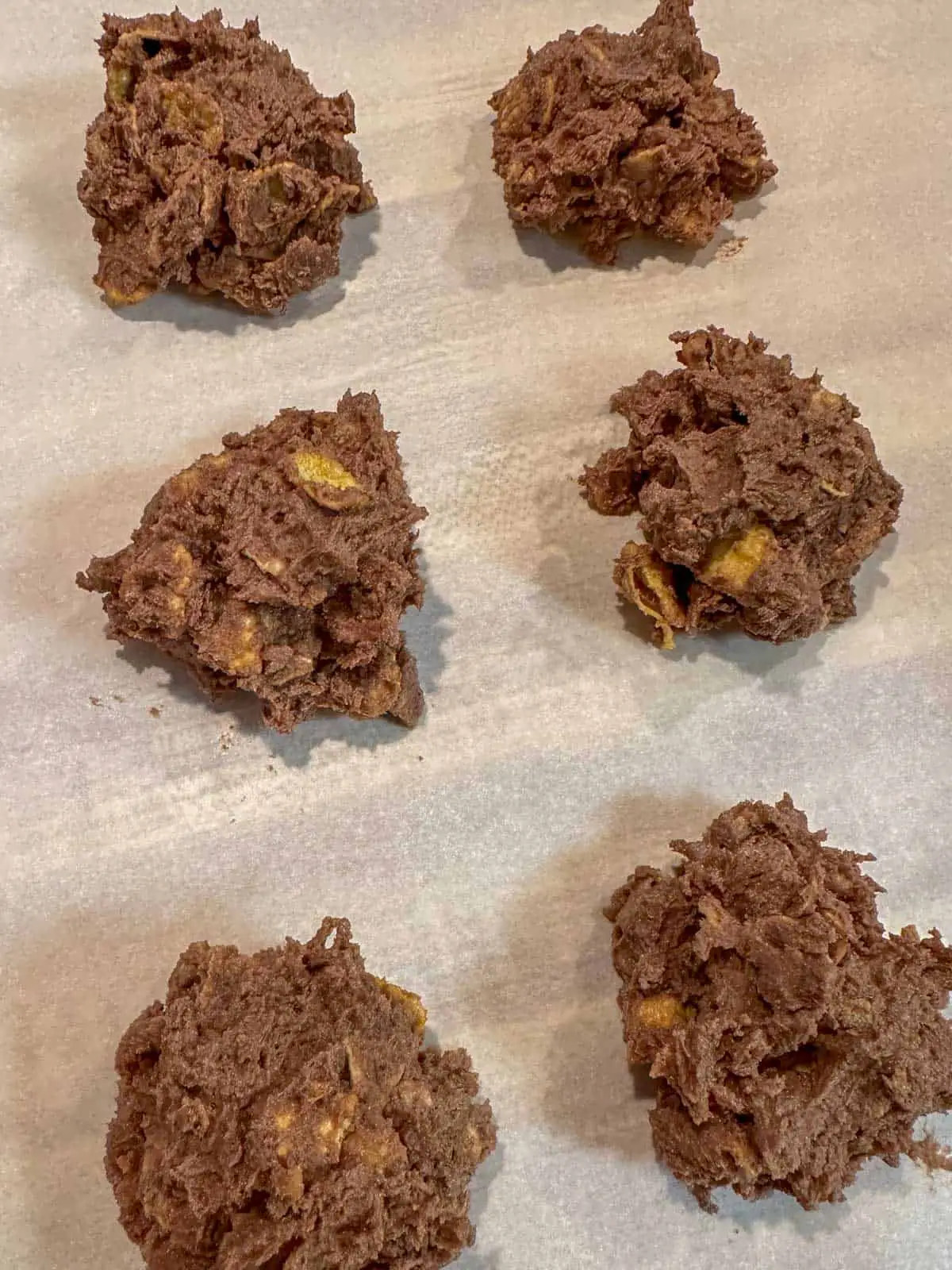 Chocolate Afghan cookie dough with cornflakes shaped into small balls and placed on parchment paper.