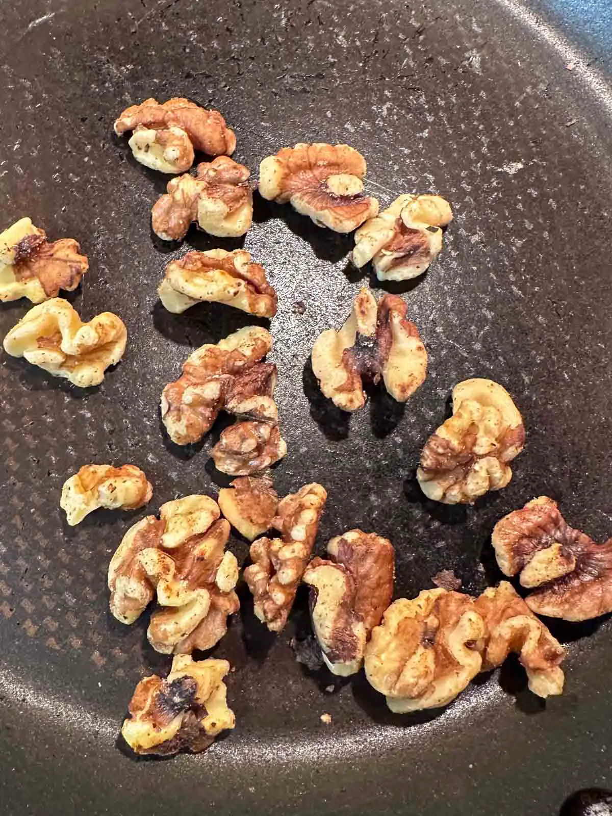 Toasted half walnuts in a skillet.